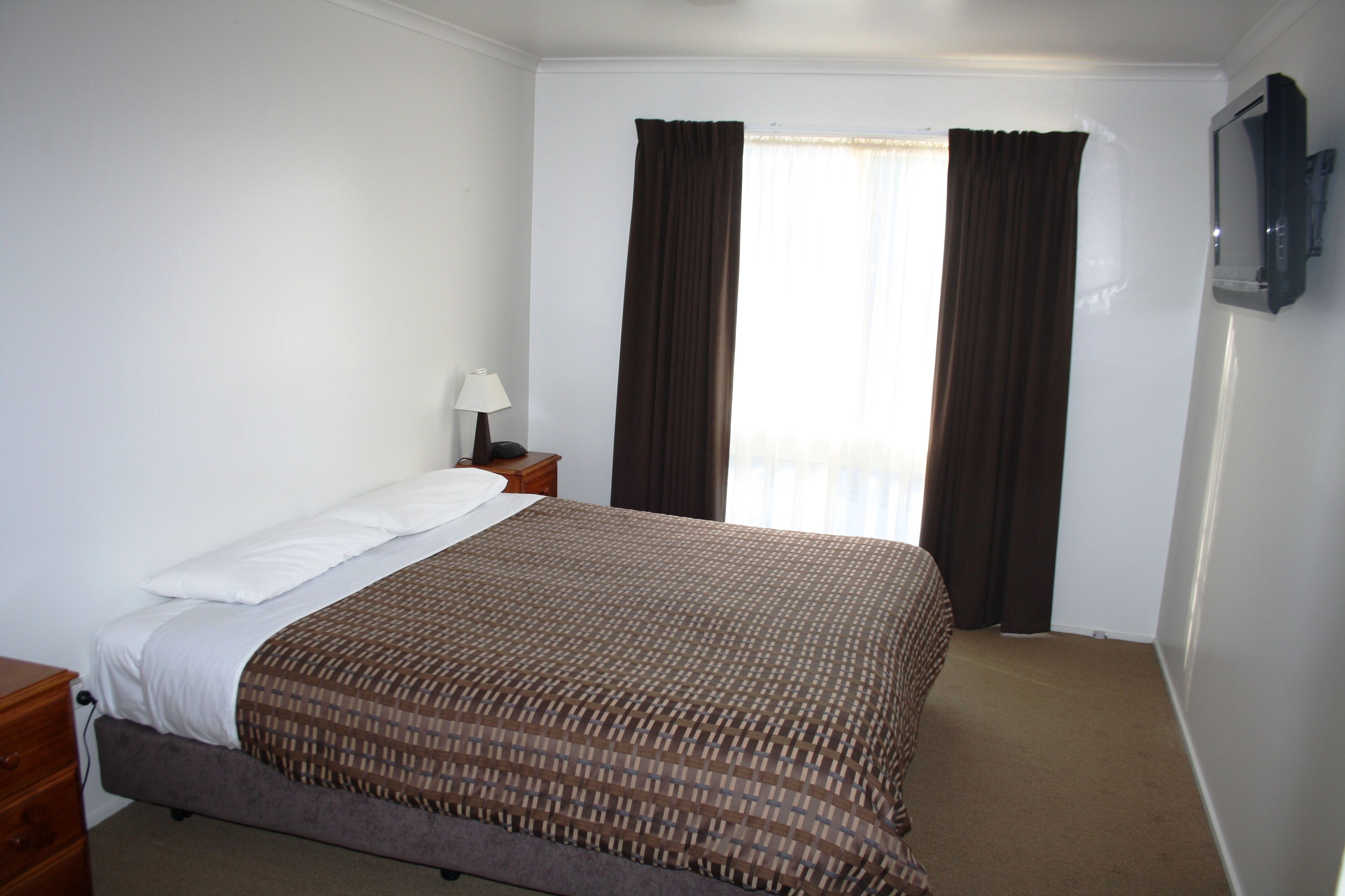 A hotel room with a bed, a nightstand, a lamp, a TV, and a window with curtains.