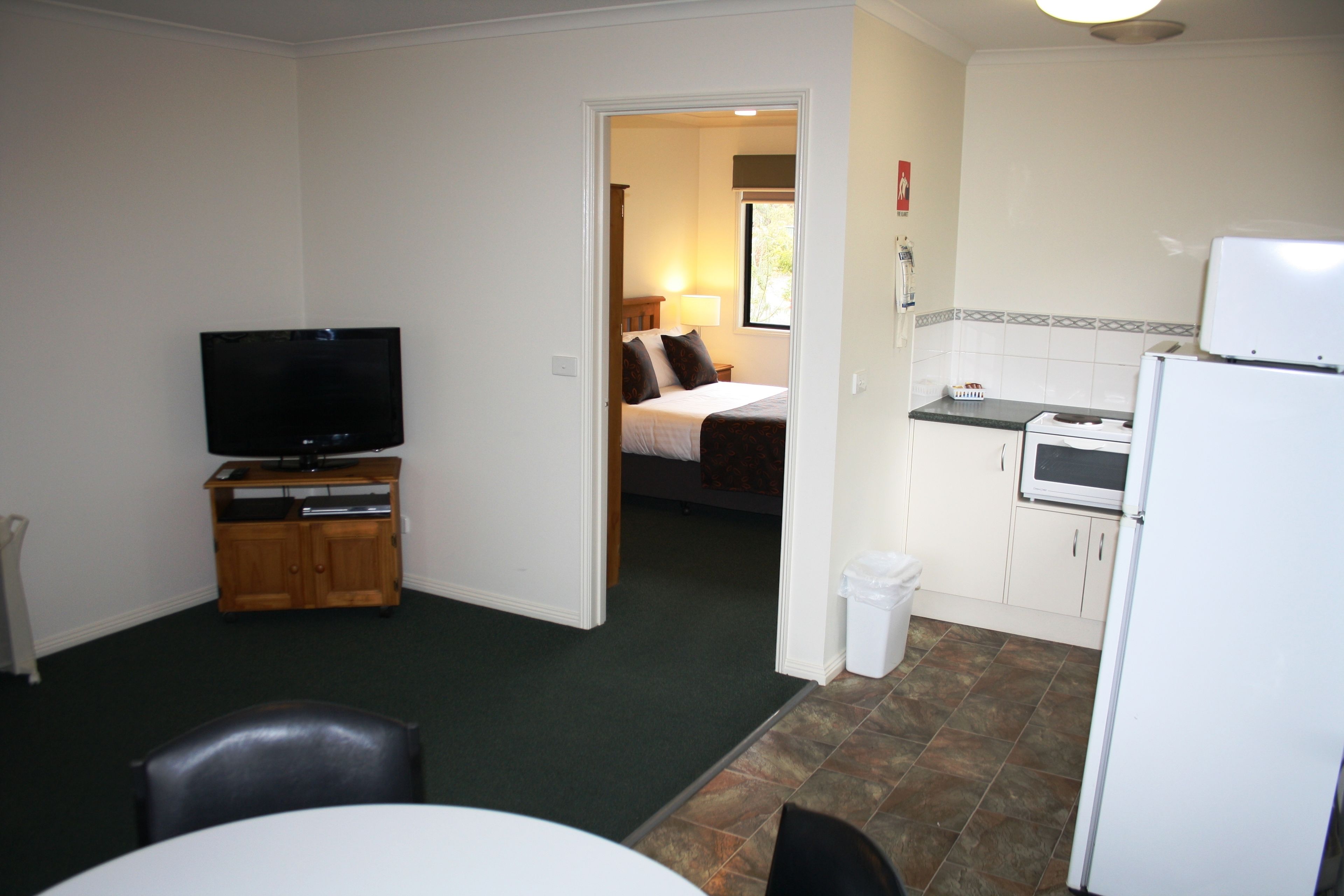 A compact room with a television, a dining table, and a kitchenette.