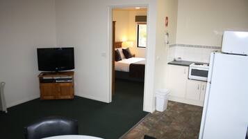 A compact room with a television, a dining table, and a kitchenette.