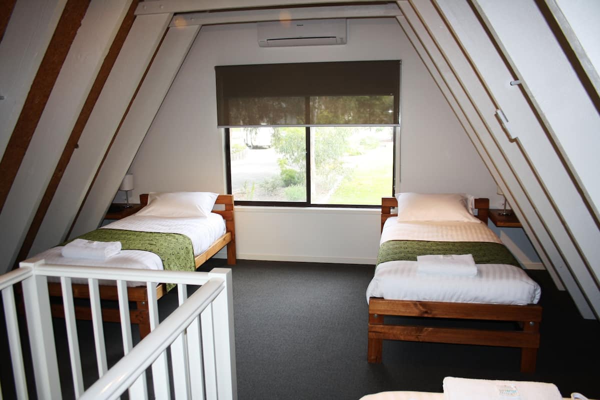 Una habitación pequeña y triangular con dos camas de madera, una ventana y una cuna blanca.