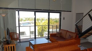A modern living room with a large sliding glass door leading to a balcony, a sofa, a small table, and a chair. - City West Accommodation (Perth)