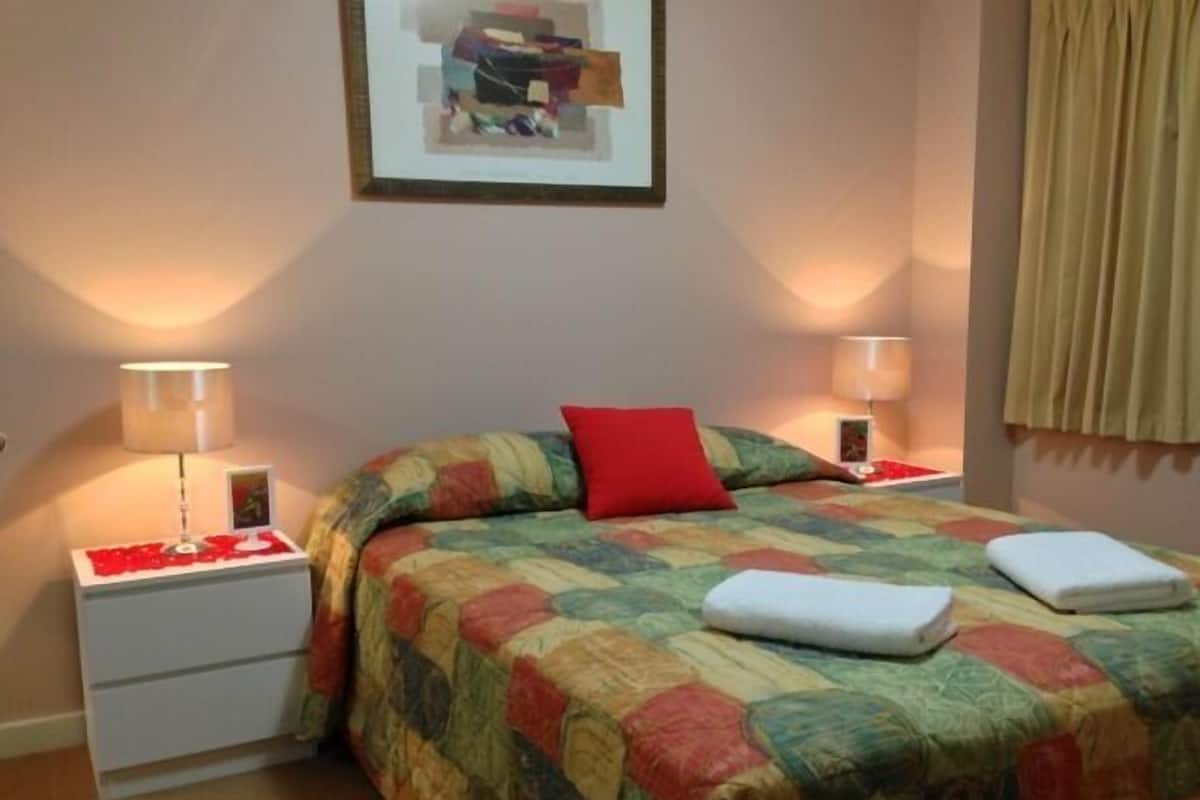 A neatly made bed with a colorful quilt, two bedside lamps, and a framed picture on the wall.