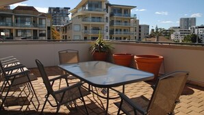 A rooftop terrace with a table and chairs, potted plants, and a view of surrounding buildings. - City West Accommodation (Perth)
