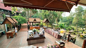 An outdoor dining area with tables and chairs, surrounded by lush greenery and traditional wooden structures. - Pung Waan Kwae Noi Resort (Sai Yok)