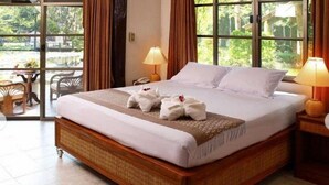 A hotel room with a large bed, two bedside lamps, a view of greenery outside, and a small table with chairs. - Pung Waan Kwae Noi Resort (Sai Yok)