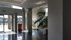 Een moderne hotel lobby met een glazen deur naar buiten, een grote potplant en een bordje met informatie over een appartementverhuur in de buurt.