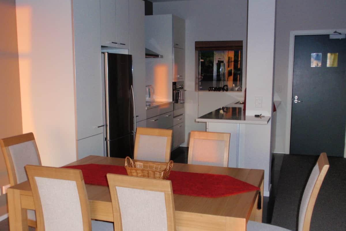 A compact kitchen with white cabinets, a refrigerator, and a microwave. There is a dining area with a wooden table and chairs, and a small window above the sink.
