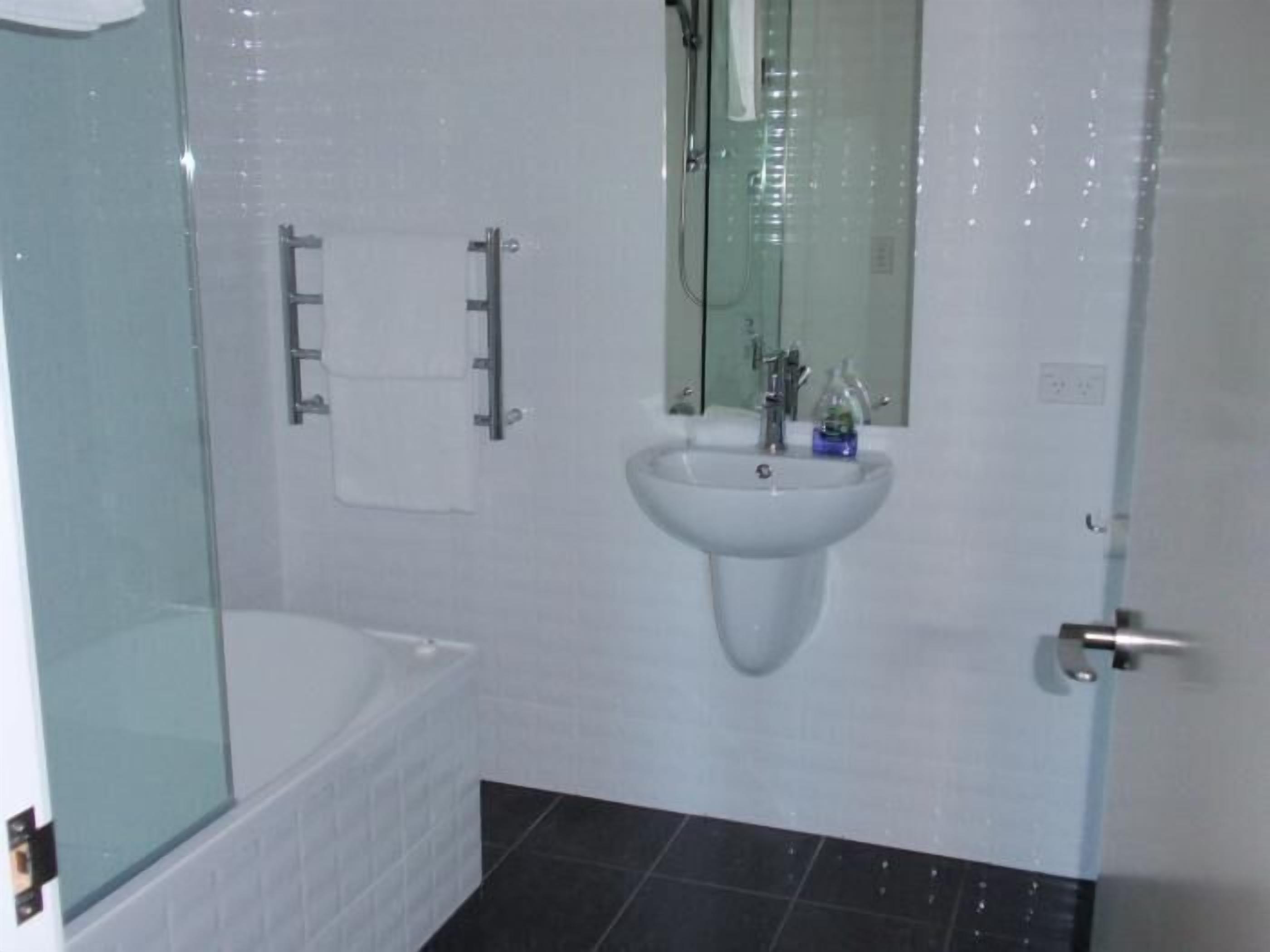 A bathroom with a glass-enclosed shower, a white sink with a mirror above it, and a white bathtub.