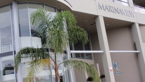 Een modern gebouw met een glazen gevel, een bord met de tekst 'MARINAVIEW' en enkele potplanten ervoor.