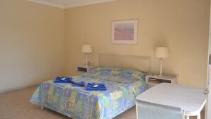 A room with two beds, each with a blue and yellow patterned bedspread, two bedside tables with lamps, and a small table with a white tablecloth. - South Hedland Motel (South Hedland)