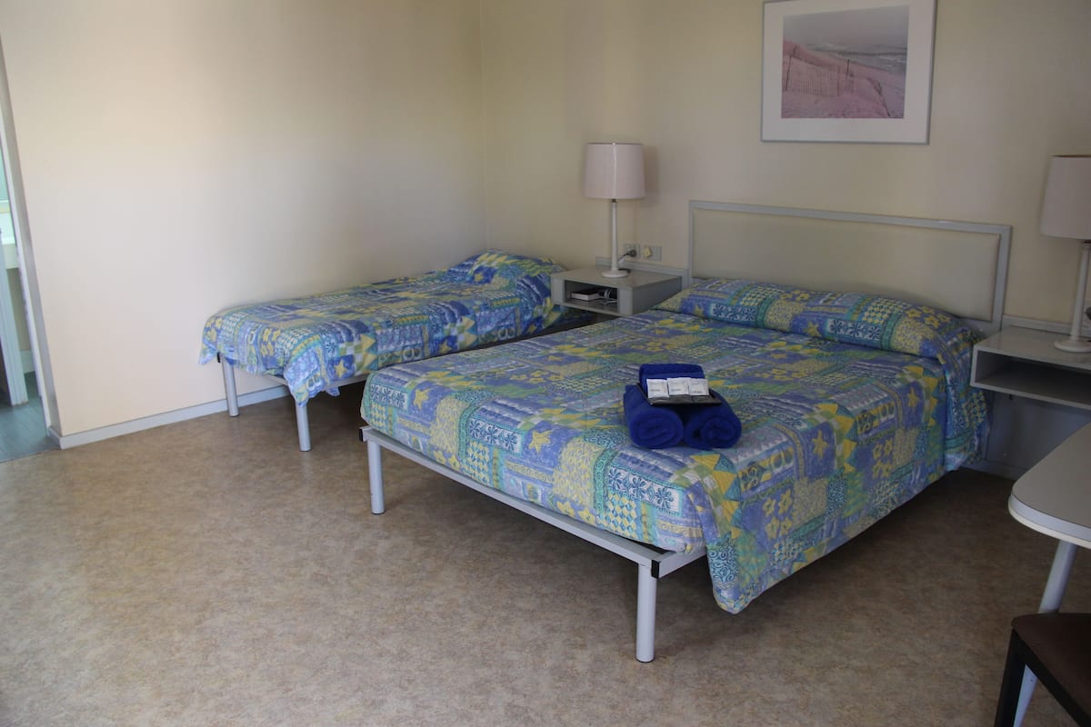 Ein Hotelzimmer mit zwei Einzelbetten, einem kleinen Tisch, einem Nachttisch und einer Lampe.