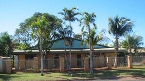 A two-story building with a green roof, surrounded by palm trees and a metal fence. - South Hedland Motel (South Hedland)