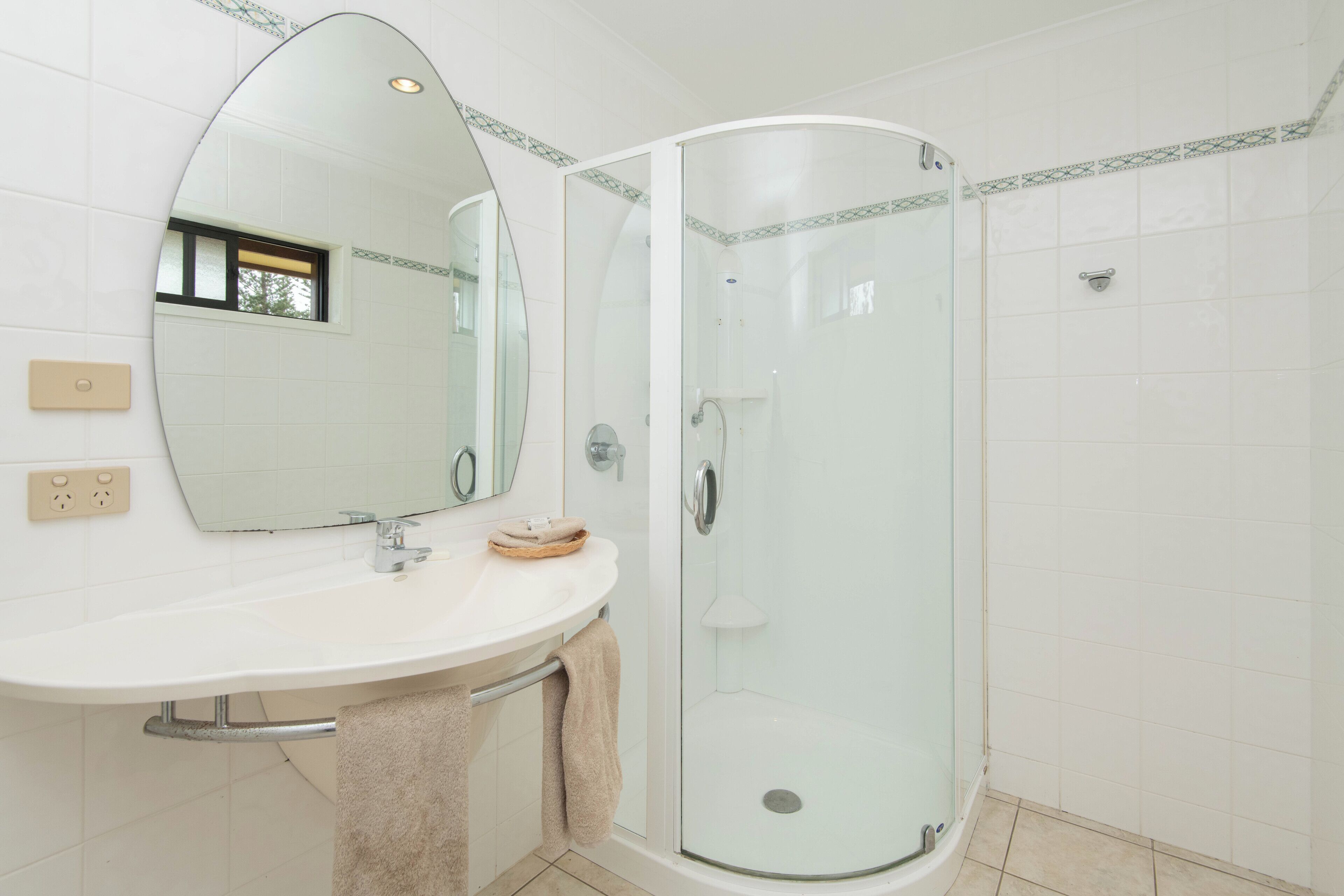 Une salle de bain moderne avec une douche à parois en verre incurvées, un lavabo blanc avec un miroir et une serviette beige.