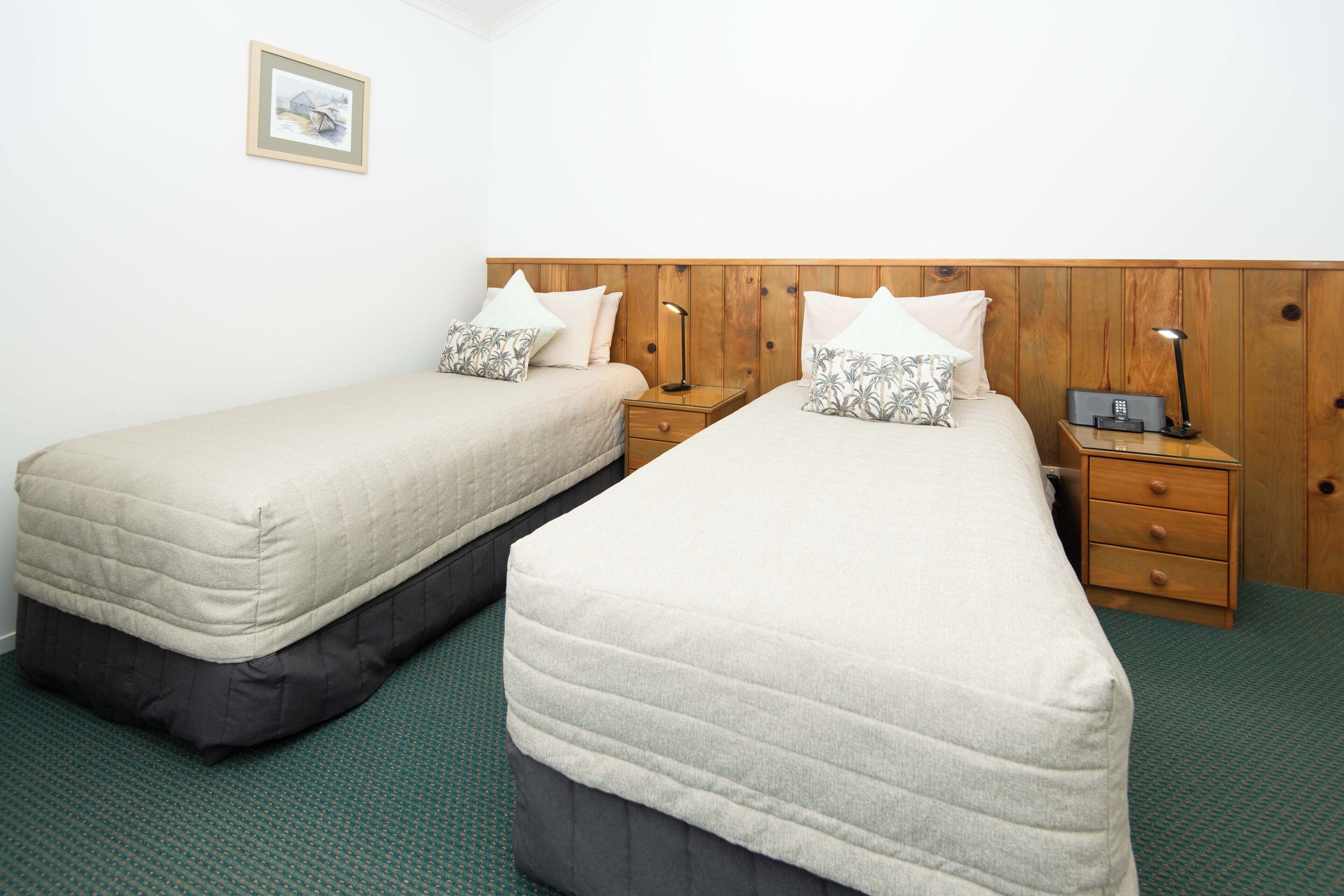 A twin room with two single beds, wooden headboard, bedside tables, and a small bedside lamp.
