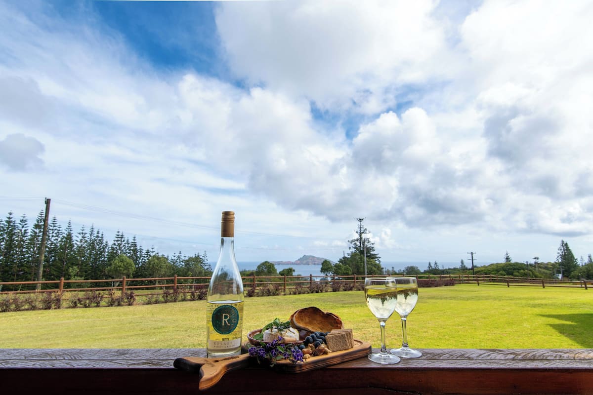 A table with a bottle of rosé wine, a glass of white wine, cheese, bread, and a wooden tray with flowers.