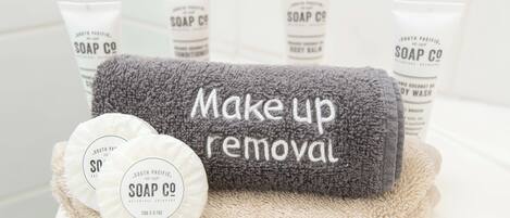 Une salle de bain équipée d’une serviette grise sur laquelle est inscrit « pour enlever le maquillage » et de deux savons ronds présentés dans des contenants portant la marque « SOAP CO ».