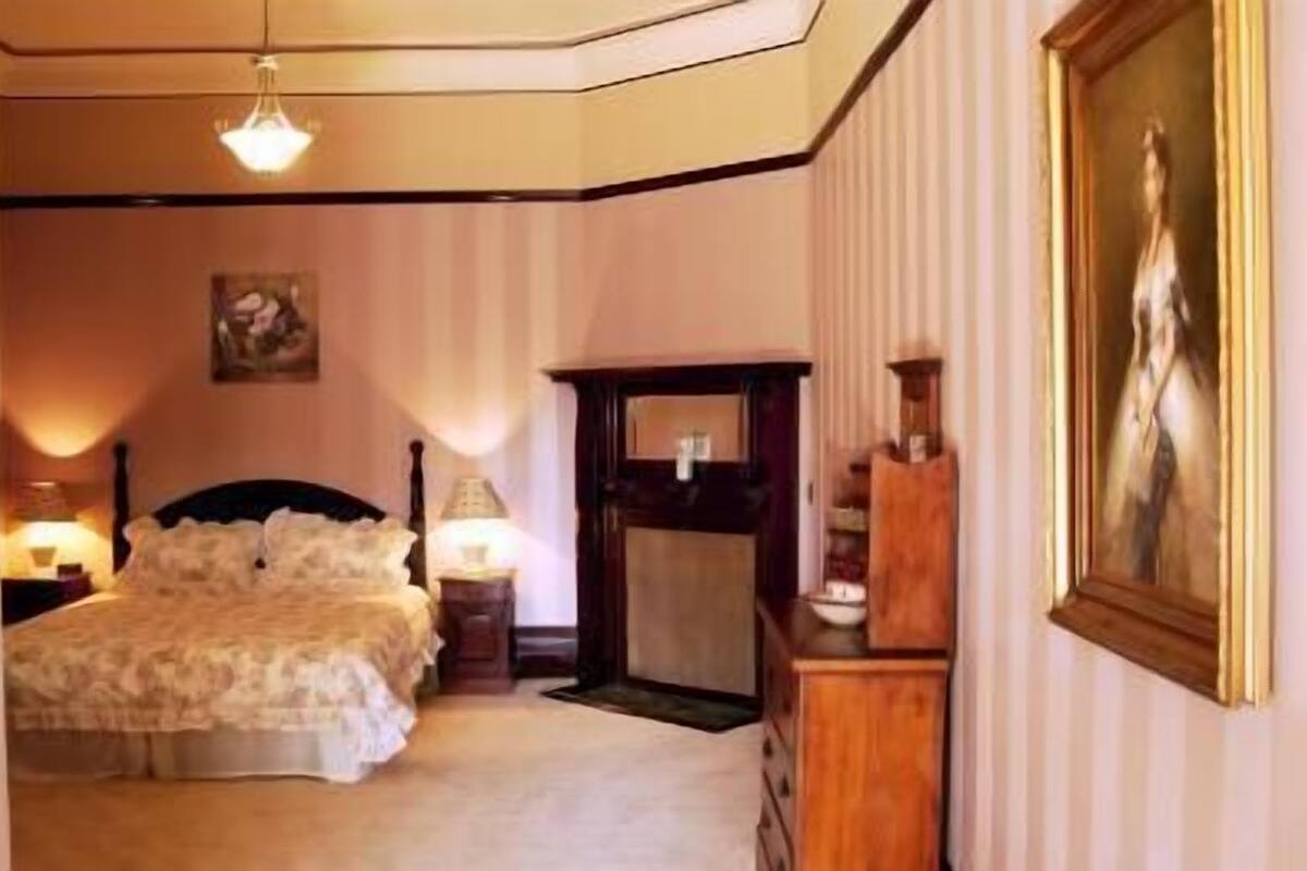 A bedroom with a bed, bedside lamps, a dresser, and a painting on the wall.