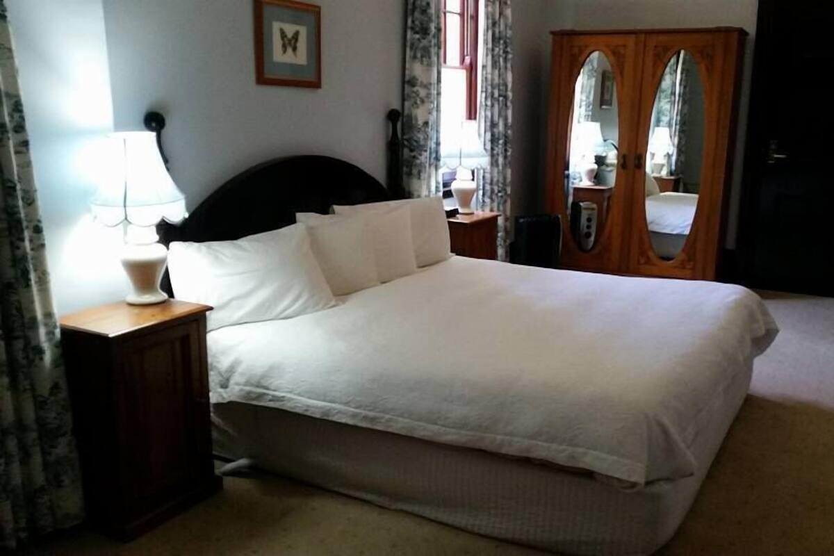 A neatly made bed in a hotel room with a wooden headboard, a bedside table with a lamp, and a mirror on the wall.