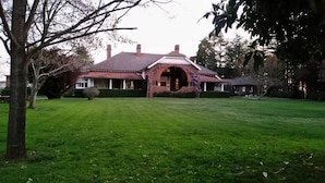 A large, single-story house with a prominent arched entrance, surrounded by a well-maintained lawn and mature trees. - Petersons Armidale Winery & Guesthouse (Armidale)