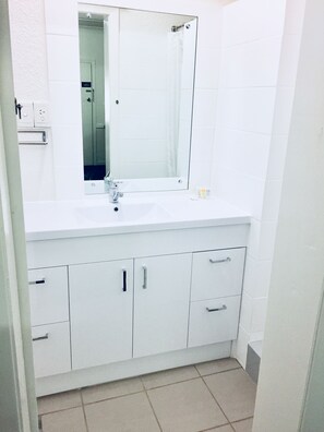 A bathroom with a white sink, mirror, and cabinets.