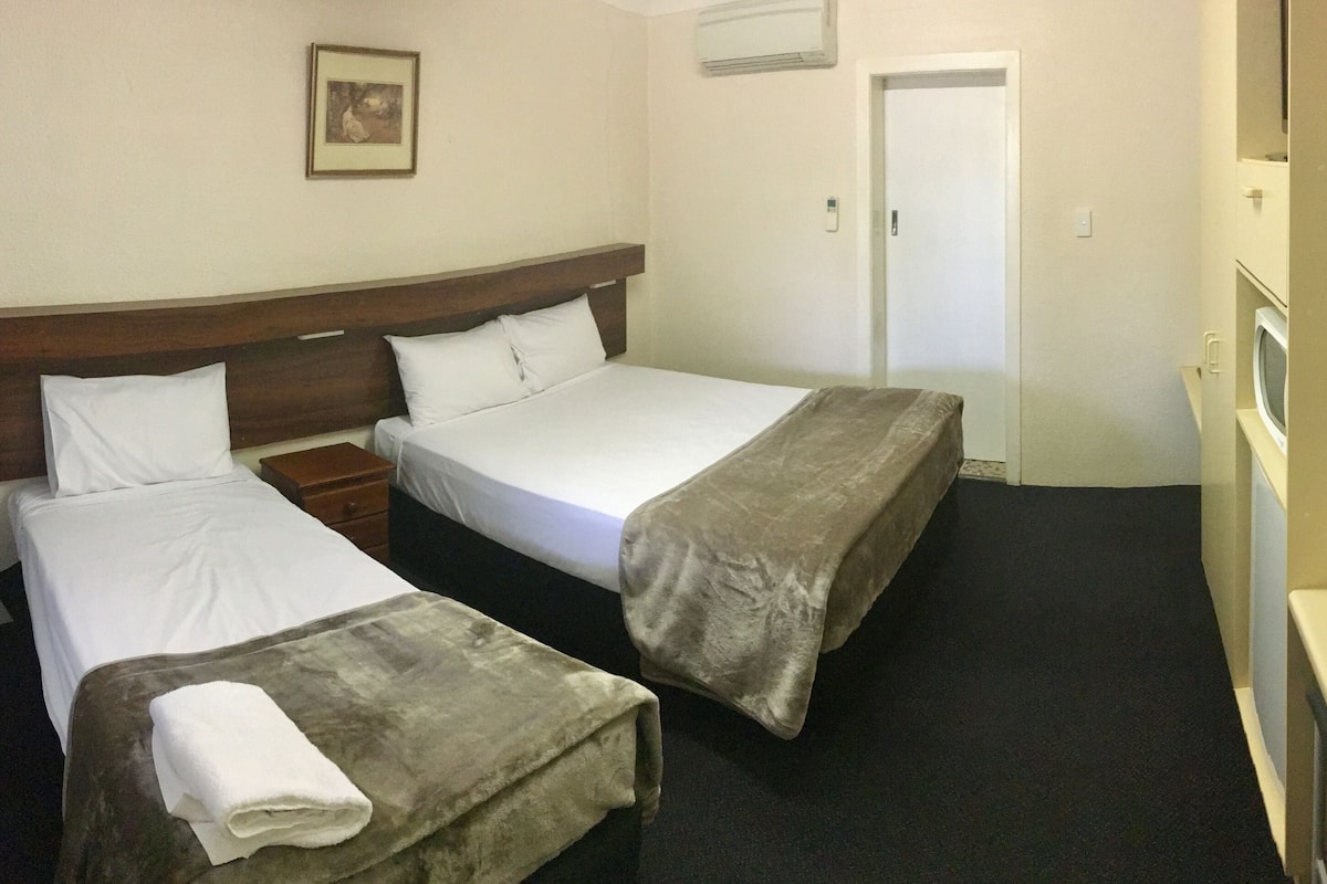 A hotel room with two beds, a bedside table, a TV, and a door.