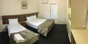 A hotel room with two beds, a bedside table, a TV, and a door.