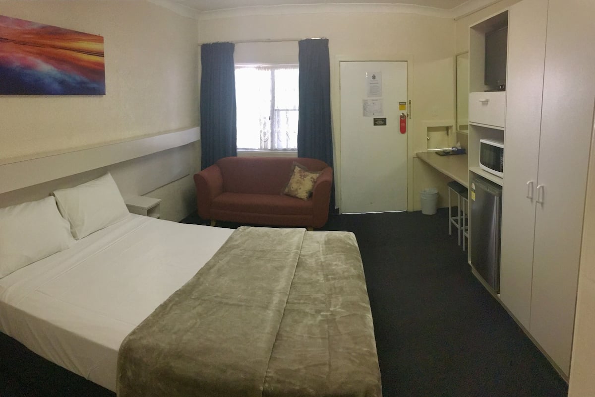 A hotel room with a bed, a sofa, a TV, a microwave, and a cabinet.