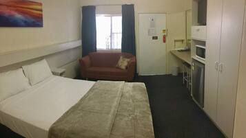 A hotel room with a bed, a sofa, a TV, a microwave, and a cabinet.