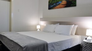 A neatly made bed with white linens, a grey throw blanket, and two bedside lamps on a white nightstand.