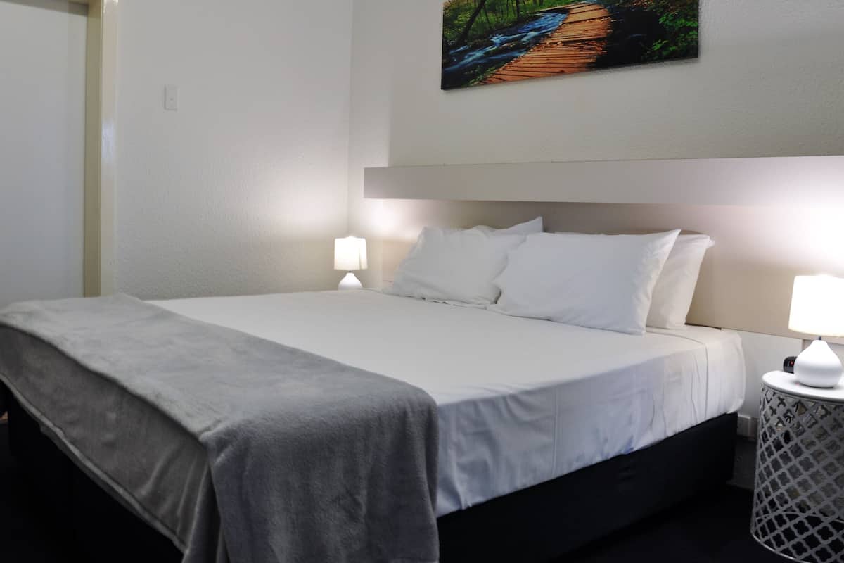A neatly made bed with white linens, a grey throw blanket, and two bedside lamps on a white nightstand.