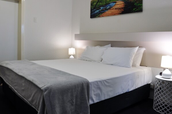 A neatly made bed with white linens, a grey throw blanket, and two bedside lamps on a white nightstand.