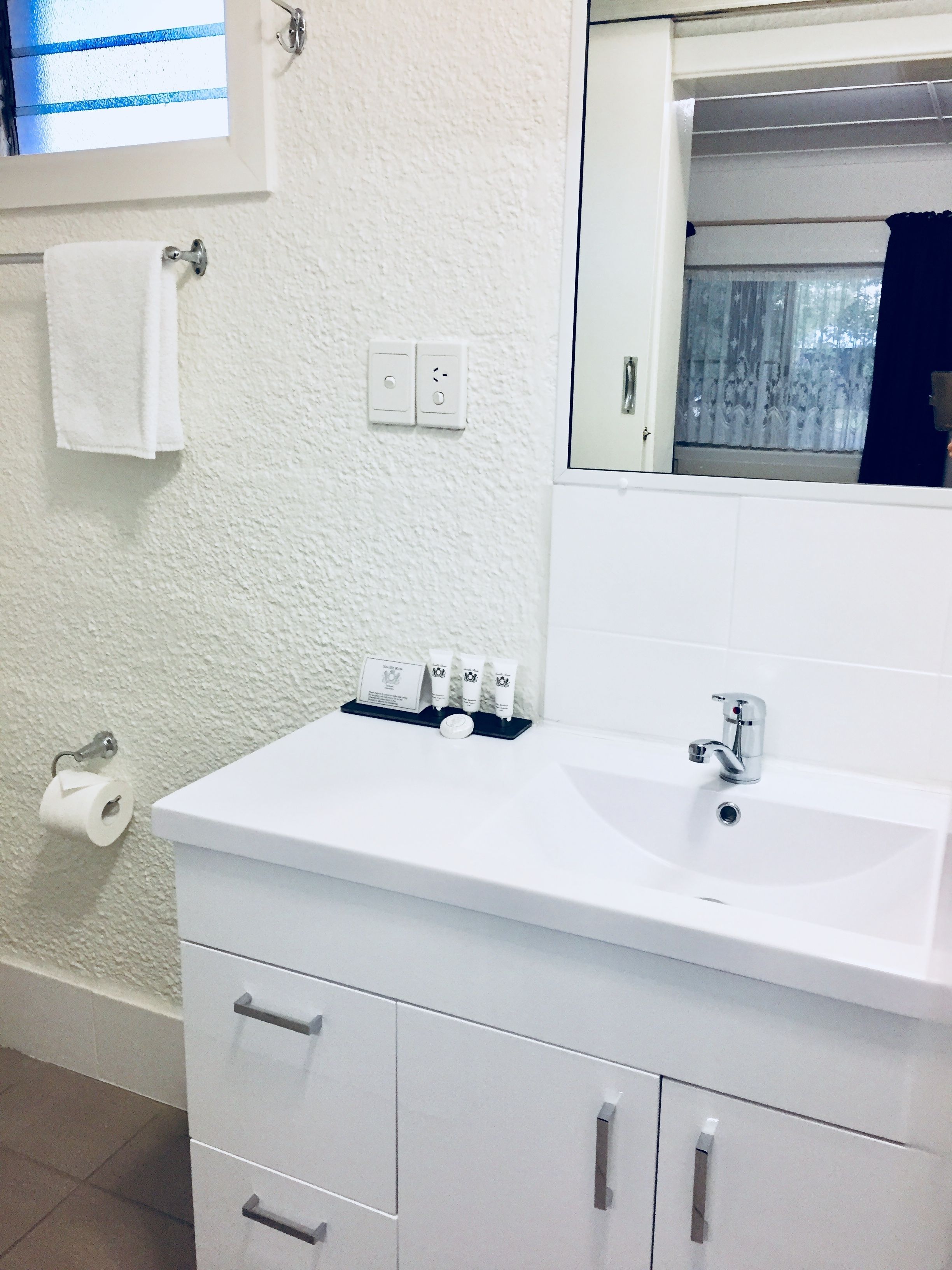 A bathroom with a white sink, a mirror, a towel rack, a toilet paper holder, and a set of toiletries.
