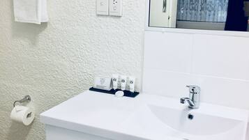 A bathroom with a white sink, a mirror, a towel rack, a toilet paper holder, and a set of toiletries.