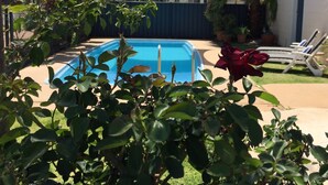 A backyard with a swimming pool, a rose bush, and a covered patio area.