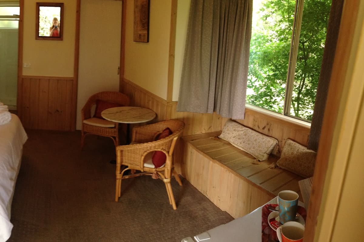Habitación de hotel con cama, una mesita, un sillón, un sofá y ventana con vista a árboles.