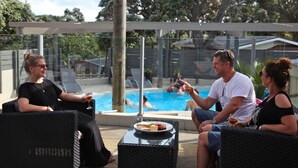 A poolside area with wicker furniture and a glass table with a plate of food.