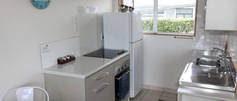 A compact kitchen with a refrigerator, stove, oven, and a window with a view.