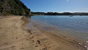 A beach with clear water, boats, and a forested hill.