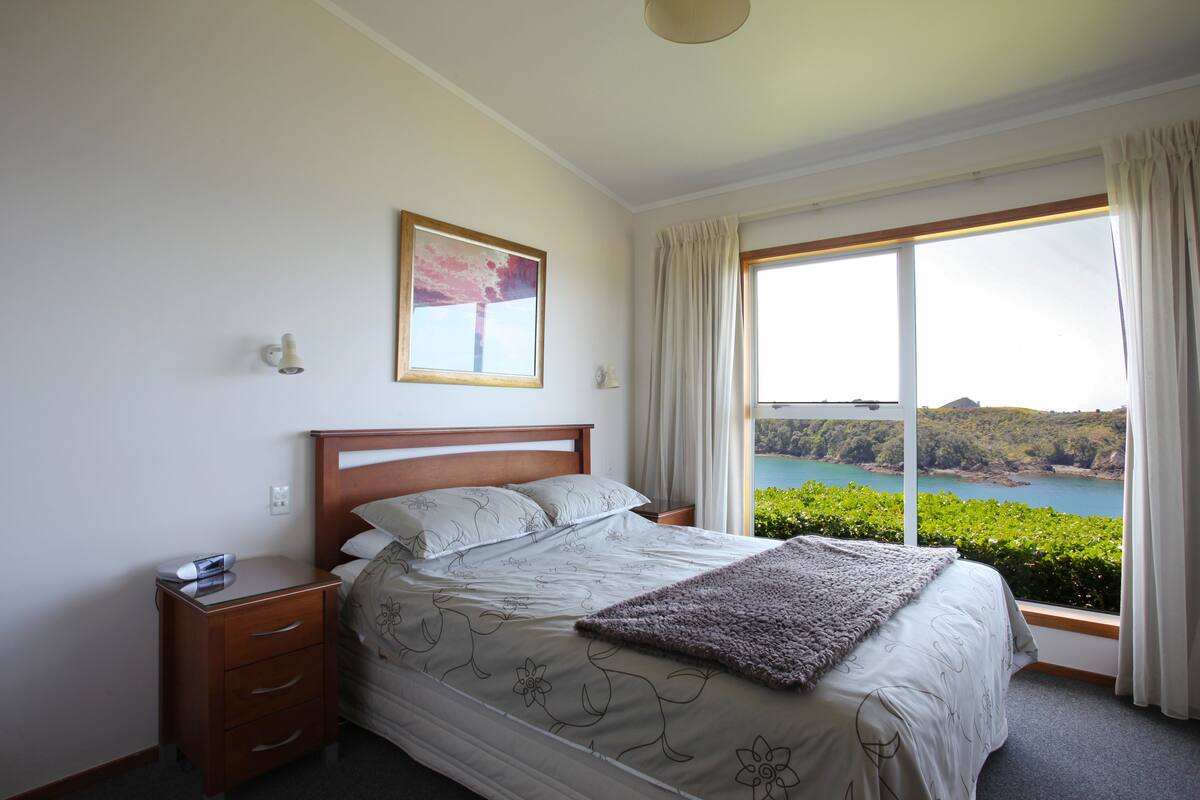 A bedroom with a large bed, a nightstand, a bedside table, a window with curtains, and a framed picture on the wall.