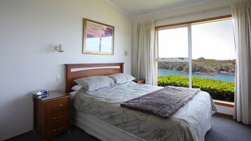 Une chambre à coucher avec un grand lit, une table de chevet, une commode, une fenêtre avec des rideaux et un tableau encadré au mur.