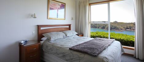 A bedroom with a large bed, a nightstand, a bedside table, a window with curtains, and a framed picture on the wall.