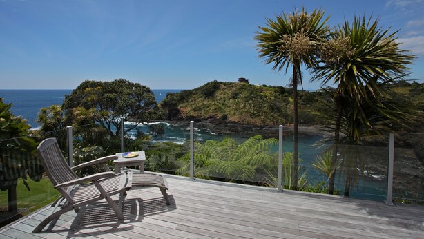 A wooden deck with two chairs and a small table overlooking a coastal landscape with a view of the sea and greenery.