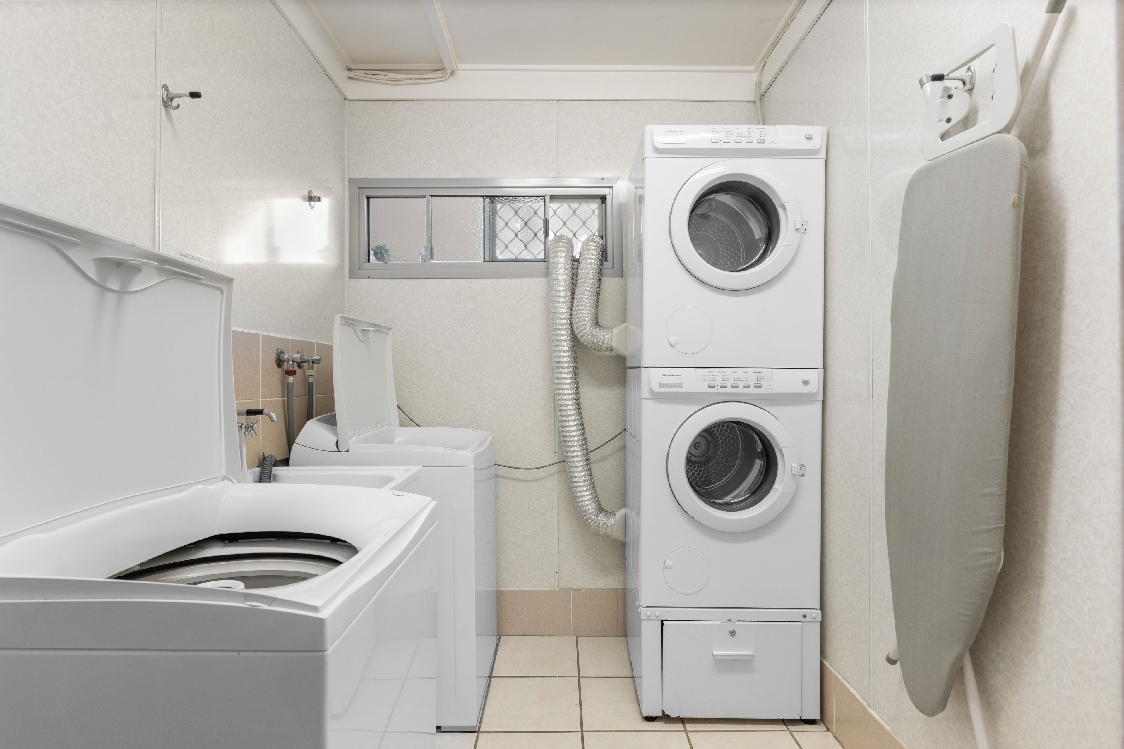 A laundry room with stacked washers and dryers, a shower area, and a window with a view.
