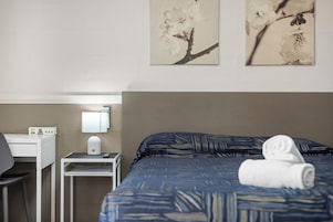 A hotel room with a bed, a desk, a lamp, and two wall-mounted paintings.