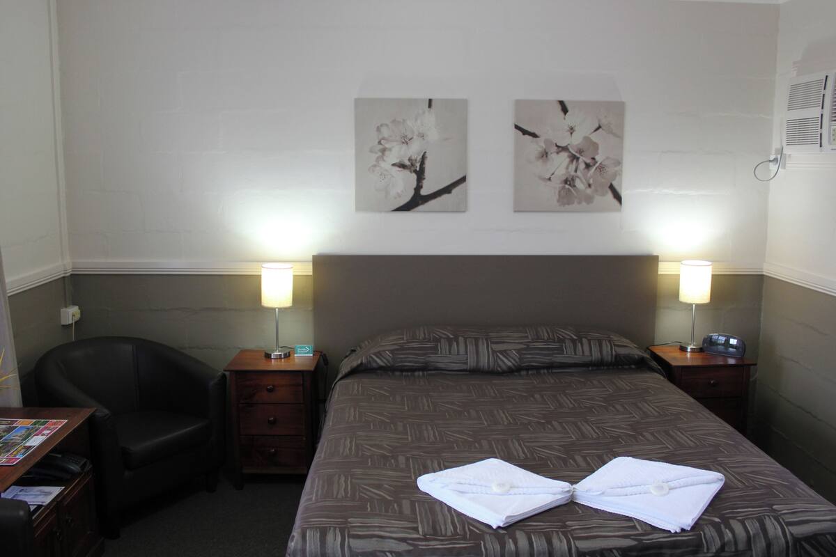 A hotel room with a bed, two nightstands, a chair, and artwork on the wall.