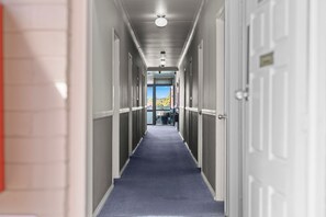 A hotel corridor with a blue carpet, white doors, and a view of a mountain landscape through the glass doors at the end. - City Motor Inn Toowoomba (South Toowoomba)