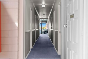 A hotel corridor with a blue carpet, white doors, and a view of a mountain landscape through the glass doors at the end.