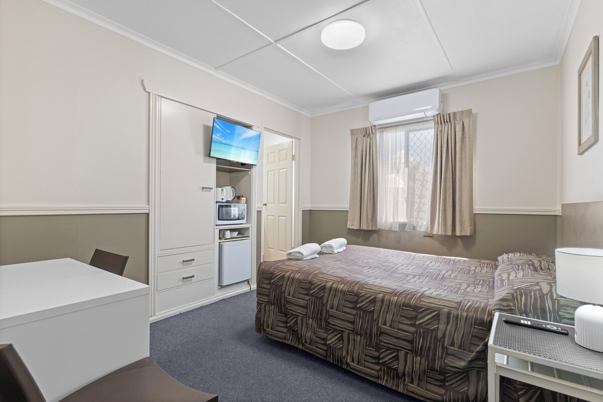 Ein Hotelzimmer mit einem Bett, einem Schreibtisch, einem Fernseher, einer Mikrowelle und einem kleinen Kühlschrank.