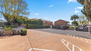 A paved driveway leading to a gated entrance with a brick building and a large tree. - City Motor Inn Toowoomba (South Toowoomba)