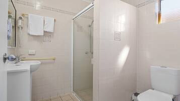 A bathroom with a shower, toilet, sink, and a towel rack.